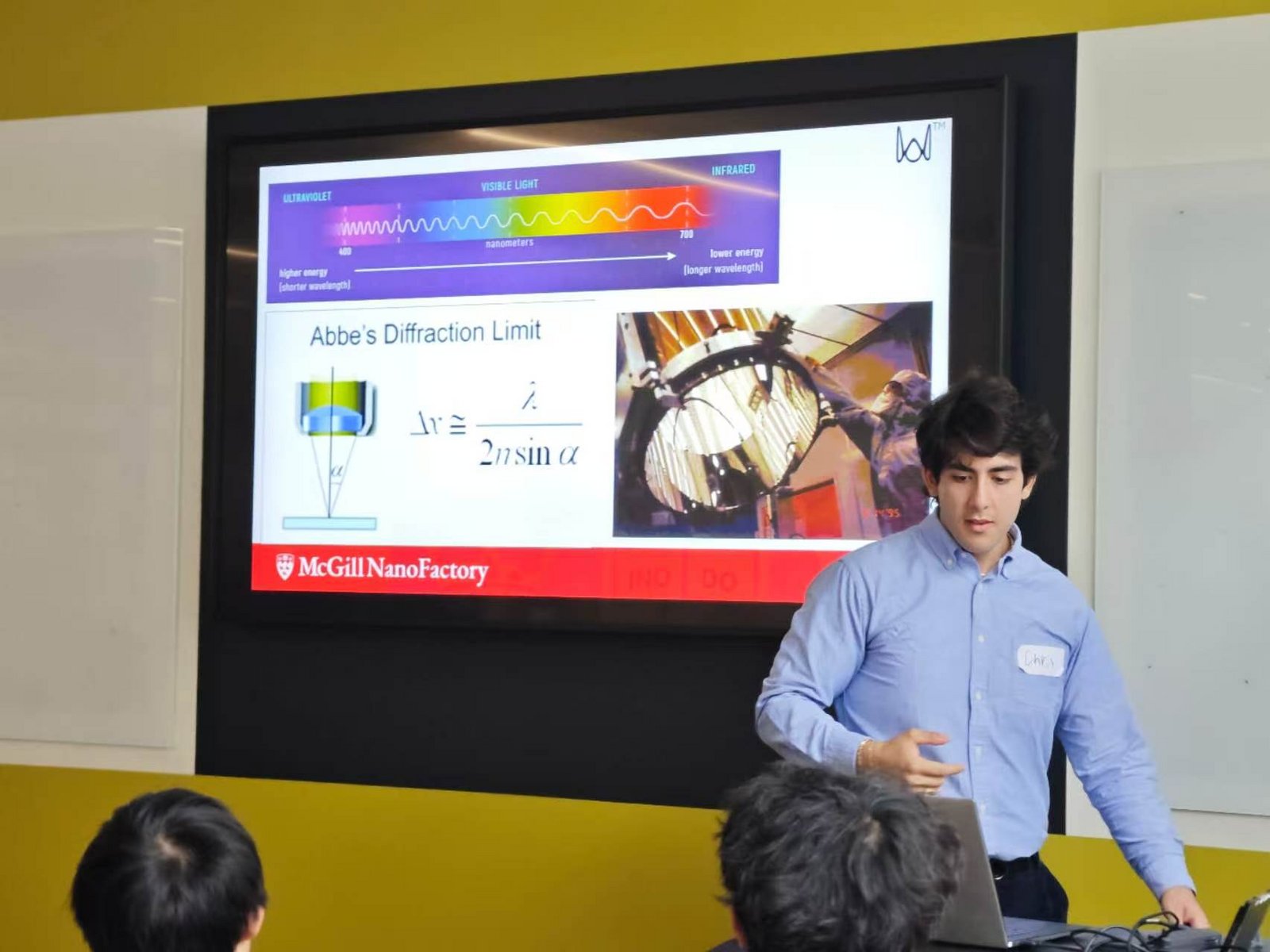 麦吉尔老师在 McGill NanoFactory 大屏前讲课（2026 年实拍） / A McGill instructor lecturing in front of the McGill NanoFactory screen (2026 camp photo)